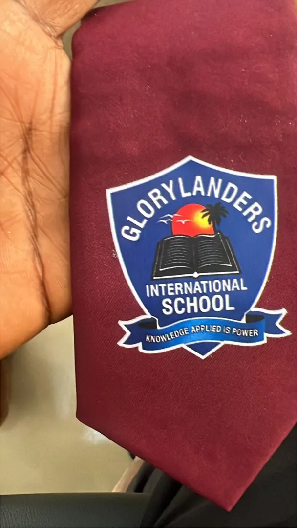 Maroon school tie with a printed Glorylanders International School shield: a blue shield with a rising sun, palm tree and open book, and the motto Knowledge applied is power